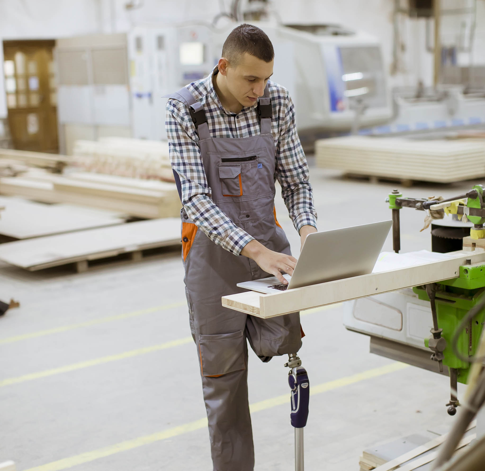 Disabled young man with an artificial leg is working at the furniture factory