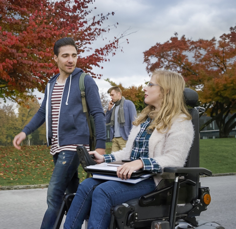 Male student talking with female student sitting on powered wheelchair at university campus