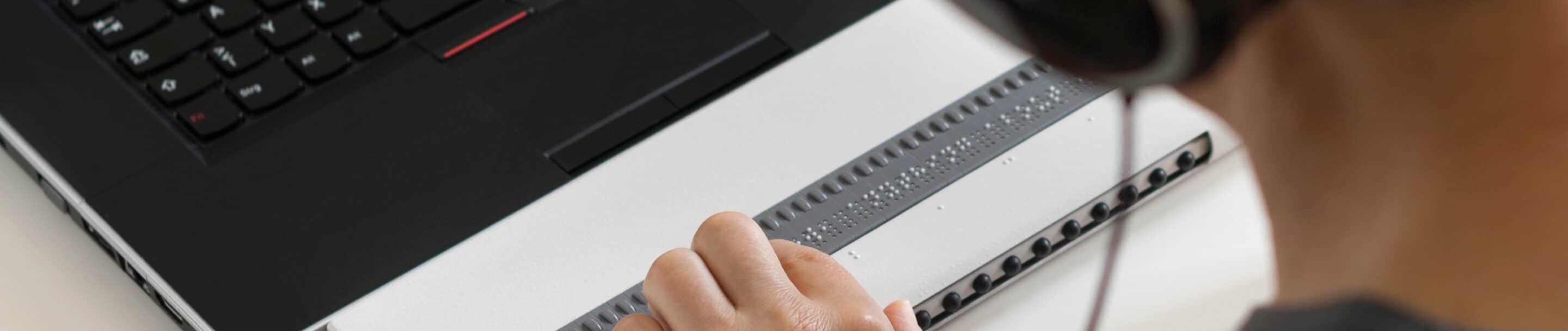 Blind person working on computer with braille display and screen