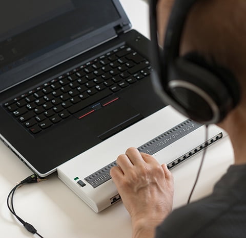 Blind person working on computer with braille display and screen